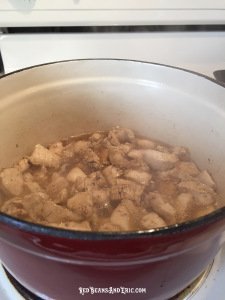 Cut pieces of boneless chicken breast being cooked in a red cast iron pot.