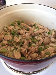 Diced onions, green bell peppers, and celery are cooked with bite-sized pieces of chicken in a cast iron pot.