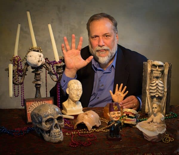 Author Michael Murphy sitting at a table with skulls and candles promoting his book Fear Dat in 2015
